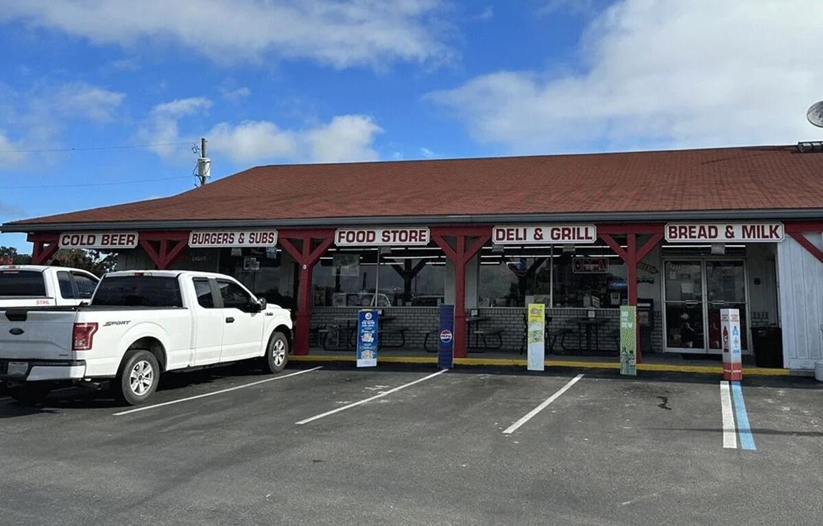Exterior view of the deli and convenience section at Gilbert’s Hardware, with signage for food, cold beer, and groceries, and trucks parked out front.