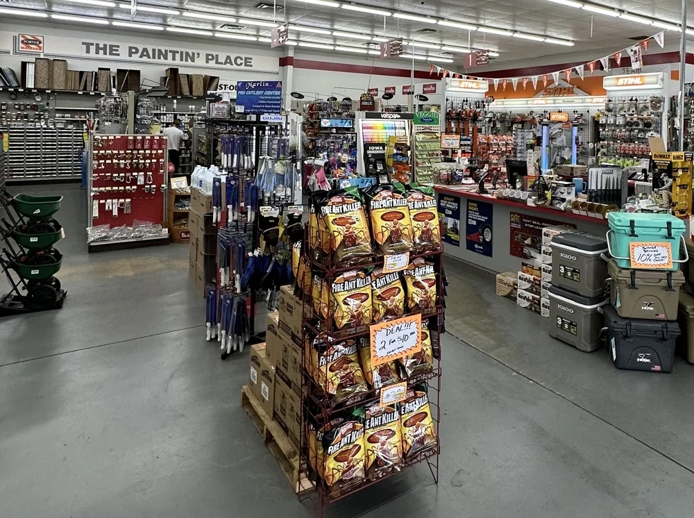 View inside Gilbert’s Hardware showing stocked shelves, tool displays, bags of fire ant killer, STIHL products, and coolers near the checkout counter.