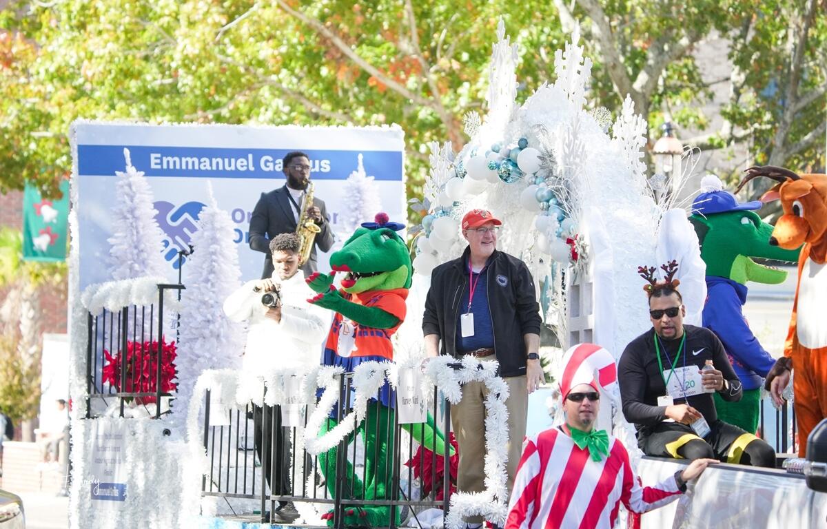 People in festive costumes and parade participants ride a holiday-themed float with balloons, white decorations, and mascots during A Very GNV Holiday Parade in downtown Gainesville.