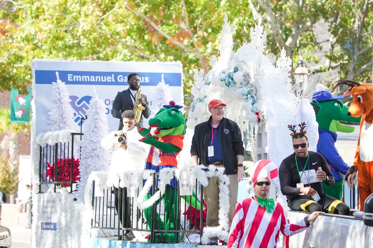 People in festive costumes and parade participants ride a holiday-themed float with balloons, white decorations, and mascots during A Very GNV Holiday Parade in downtown Gainesville.