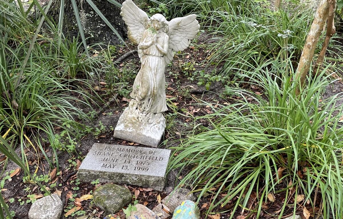 Memorial with angel statue and engraved stone for Shane Crutchfield surrounded by greenery at Squirrel Ridge Park in Gainesville, Florida.