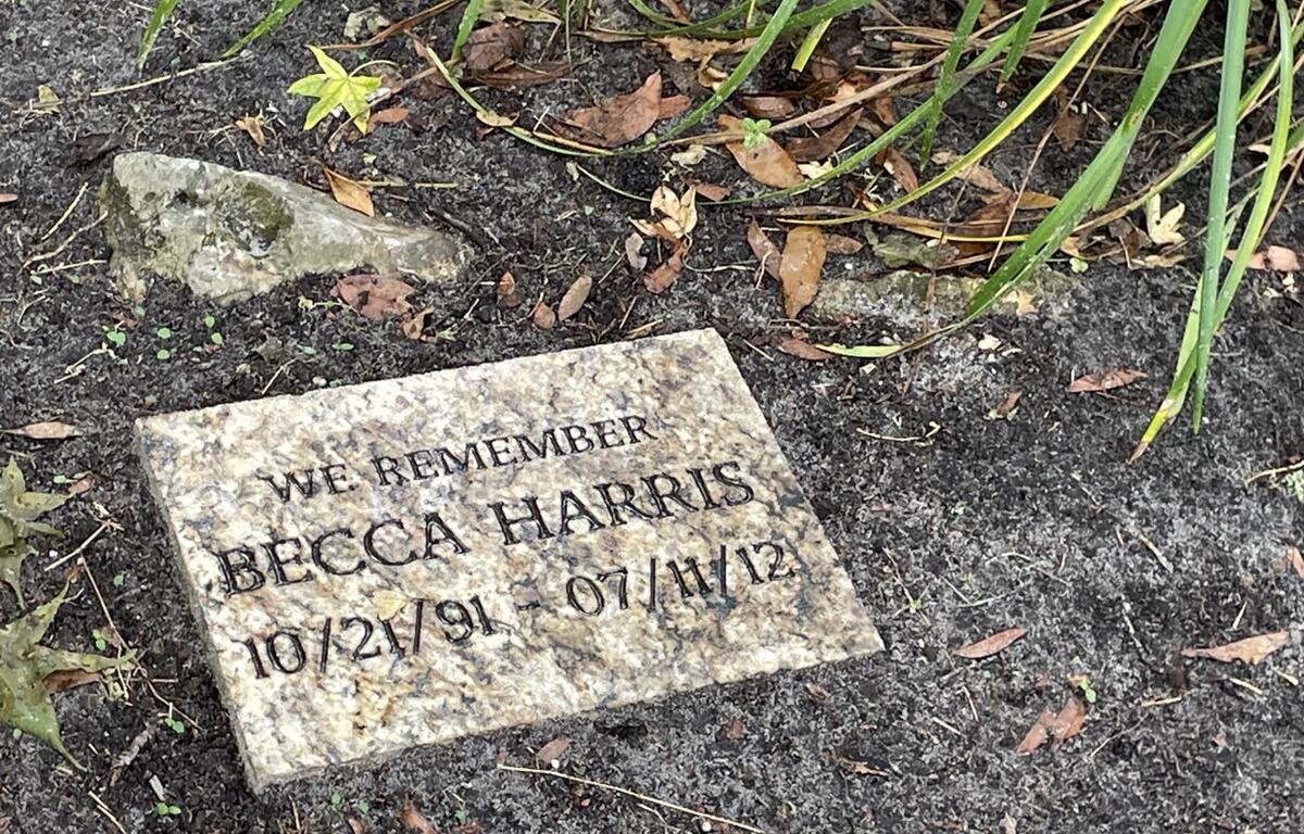 Engraved memorial stone for Becca Harris with birth and death dates, placed in the soil near greenery at Squirrel Ridge Park in Gainesville.