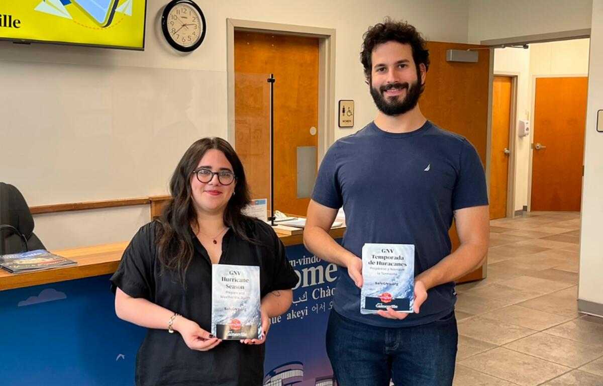 Two Gainesville staff members holding English and Spanish hurricane preparedness brochures inside a city office.