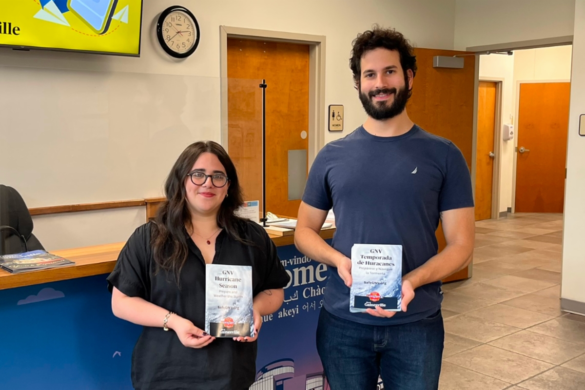 Two Gainesville staff members holding English and Spanish hurricane preparedness brochures inside a city office.