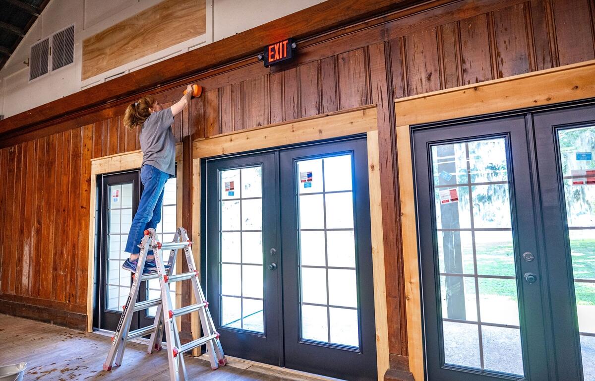 Woman on ladder cleaning wood paneling inside Heart of the Park.