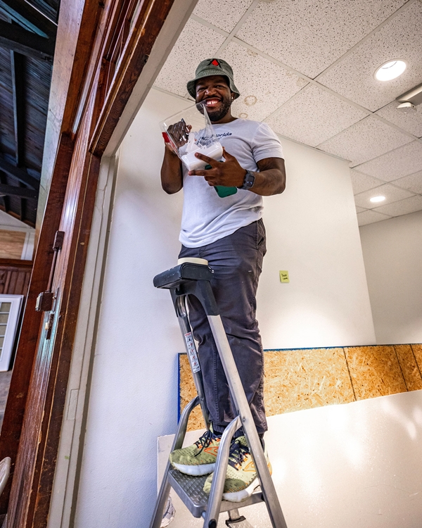 Smiling man on a ladder painting trim at Heart of the Park.