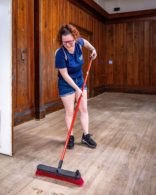 Volunteer sweeping the wooden floor inside Heart of the Park in Ocala.