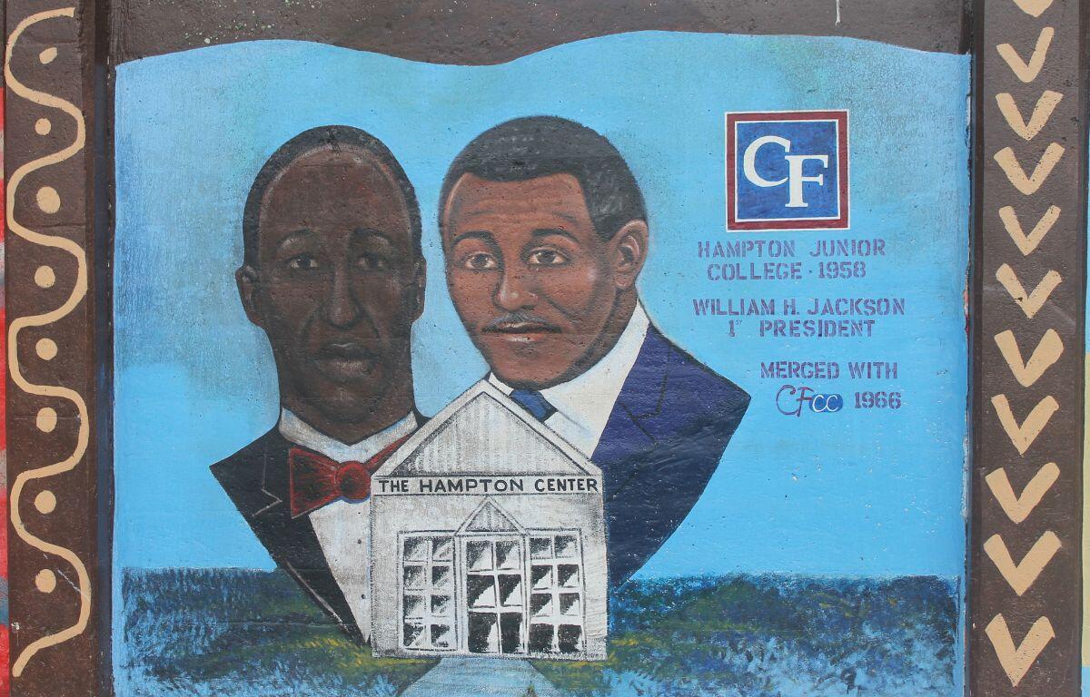 Two men standing behind a white building in front of a blue background.