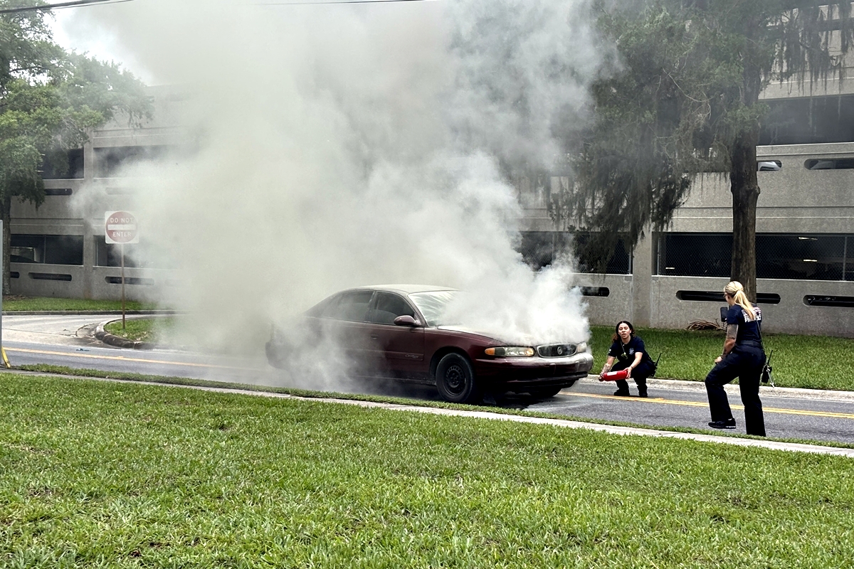 Two paramedics attempt to put out heavy smoke coming from a burning maroon car on Magnolia Extension in Ocala.