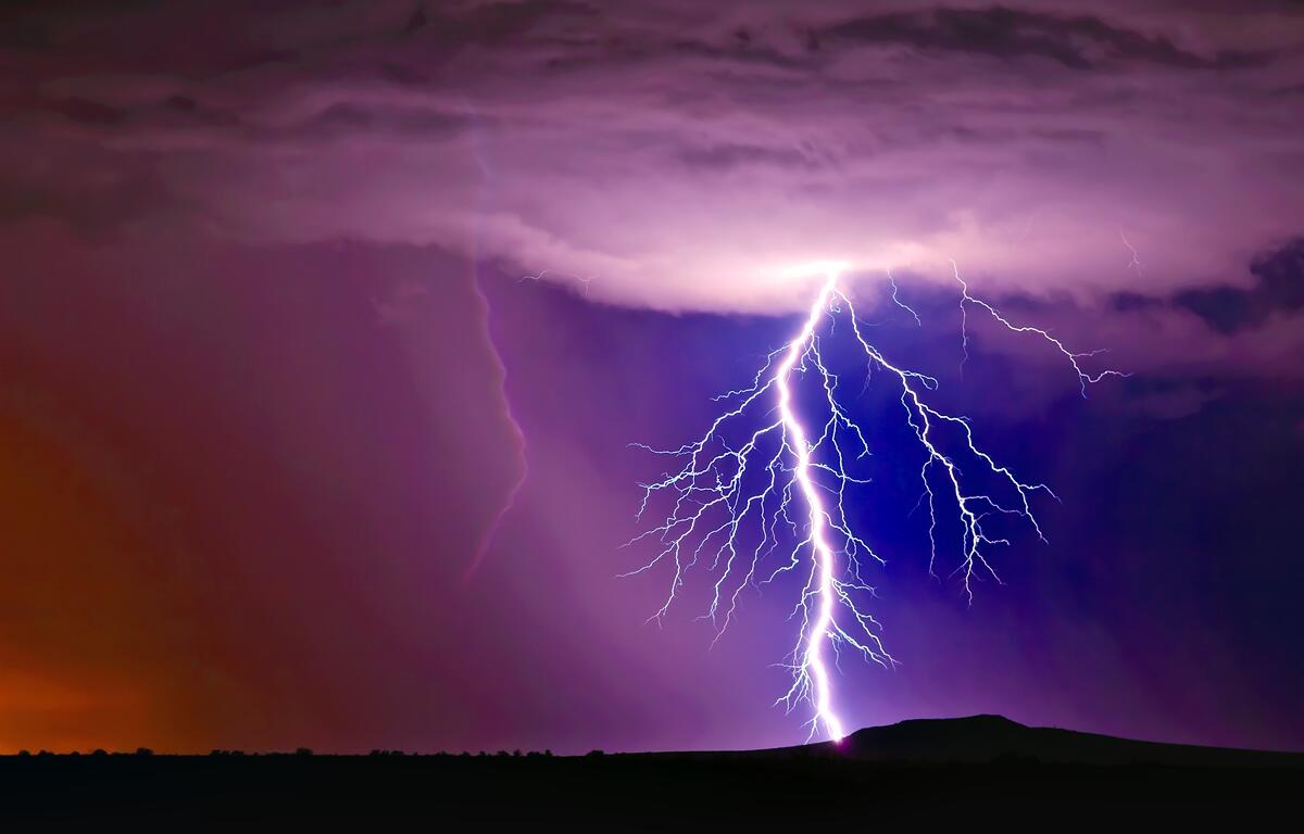 Lightning bolt flashes across the sky during a thunderstorm over a flat landscape at dusk.