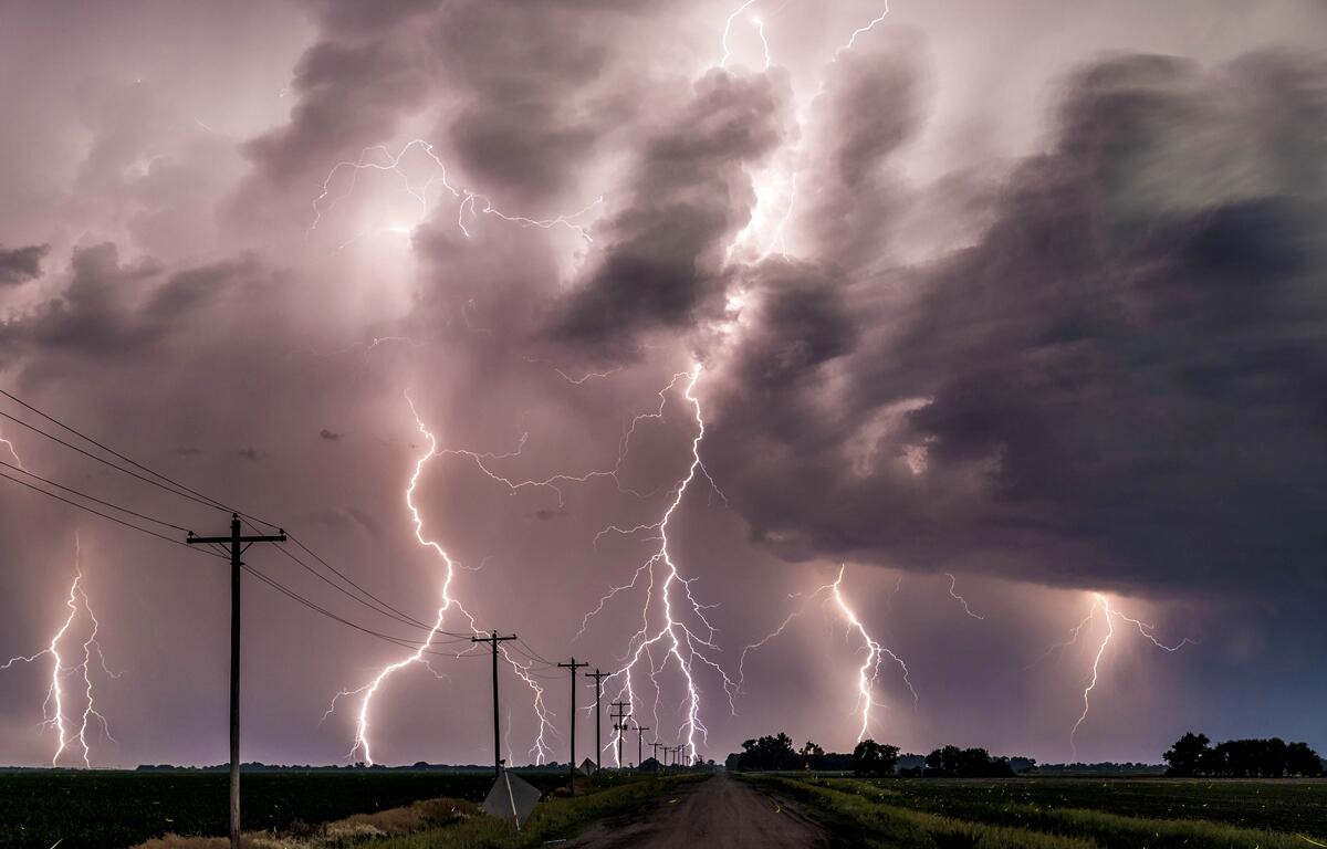 Multiple lightning bolts strike under a dark stormy sky over a rural road.