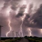 Multiple lightning bolts strike under a dark stormy sky over a rural road.