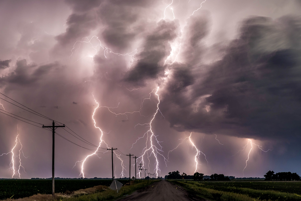 Multiple lightning bolts strike under a dark stormy sky over a rural road.