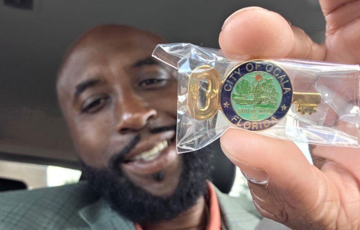 Larry Johnson smiling while holding the City of Ocala key in a small plastic package.