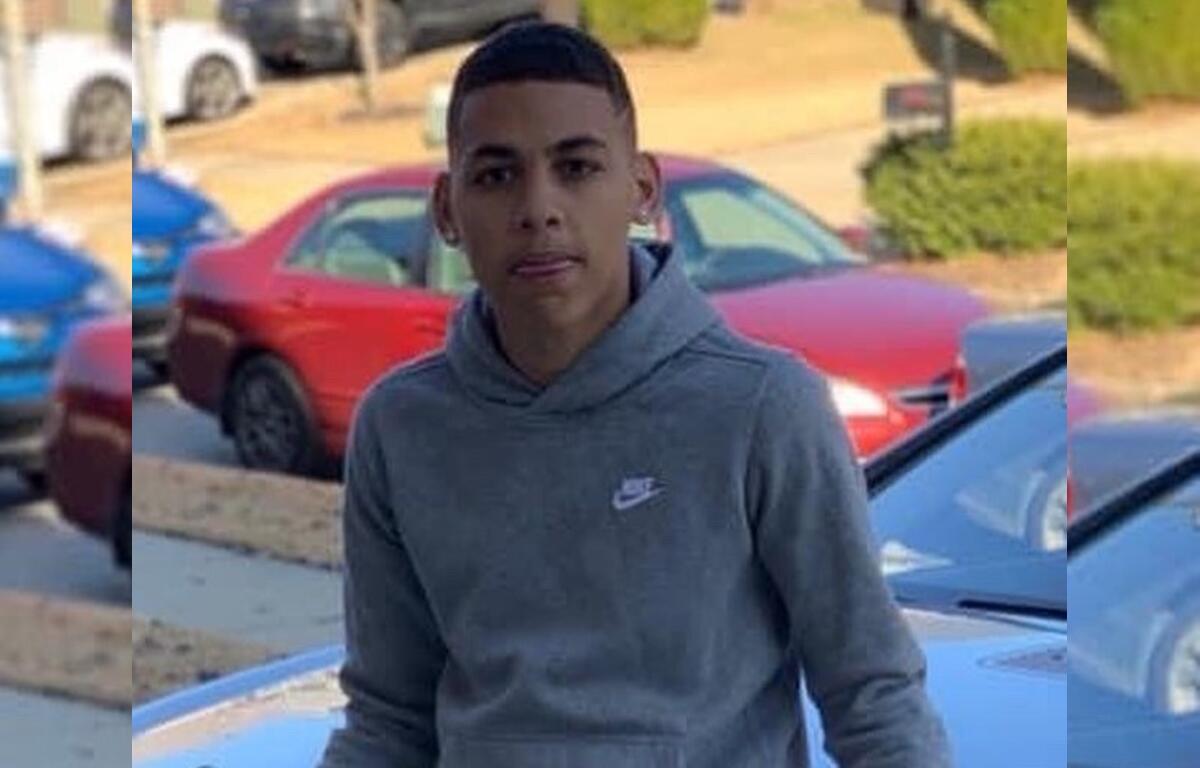 Bryson Leverette wearing a gray hoodie, standing outdoors near parked cars.