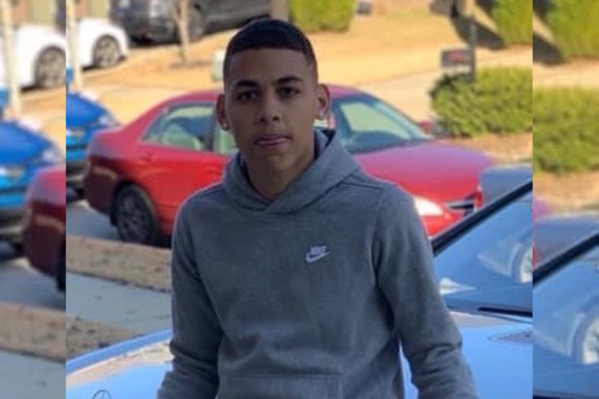 Bryson Leverette wearing a gray hoodie, standing outdoors near parked cars.