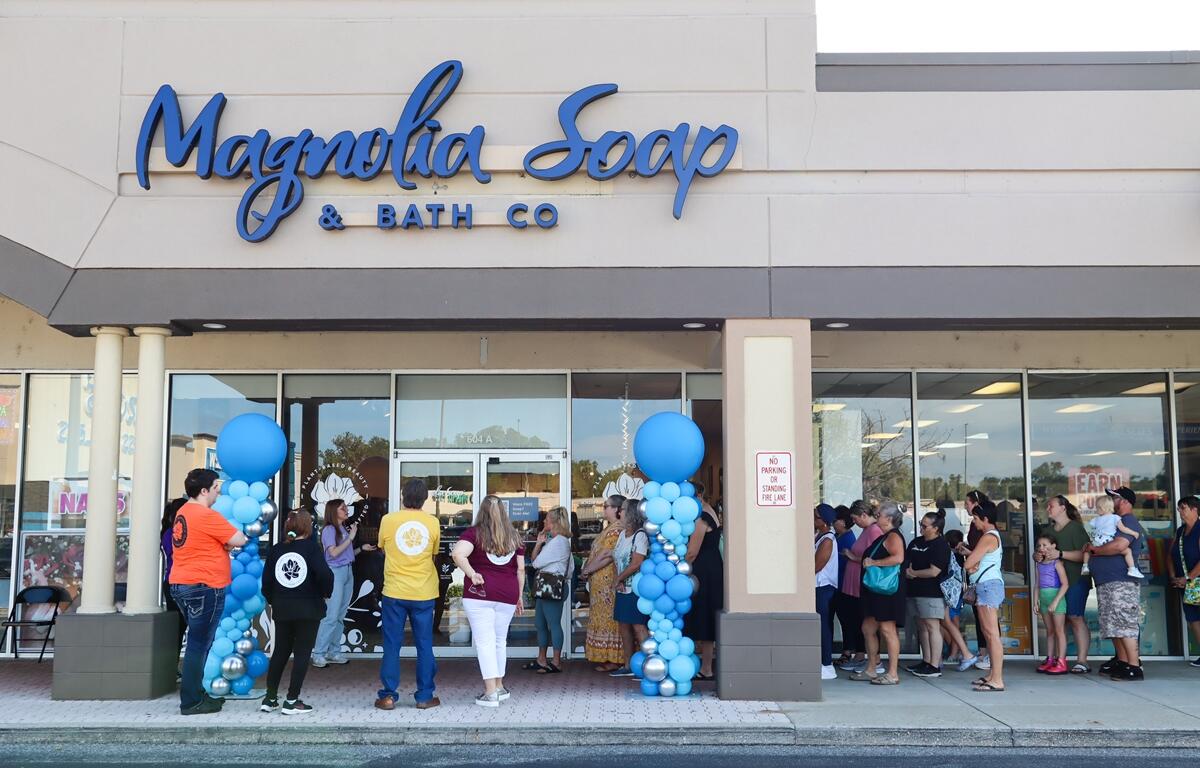 Dozens of people wait in line outside Magnolia Soap and Bath Company during the store’s grand opening, with blue balloon columns flanking the entrance in Ocala.