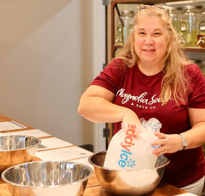 Cynthia Everett, wearing a Magnolia Soap shirt, smiles while setting up an ice bath with a bag of ice inside the store during the grand opening event in Ocala.