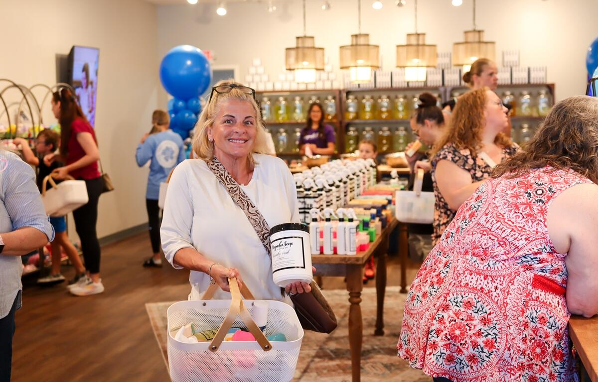 Smiling customer holding a laundry basket of soap and body care items inside Magnolia Soap and Bath Company during the grand opening event in Ocala.