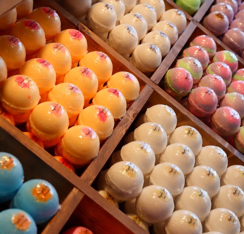 Assorted bath bombs in vibrant colors neatly arranged in wooden display trays at Magnolia Soap and Bath Company in Ocala.
