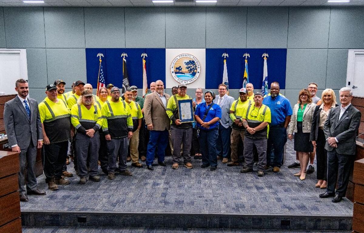 Marion County commissioners and Solid Waste staff gather in the commission chambers for a group photo, holding a framed proclamation honoring Waste and Recycling Workers Week.