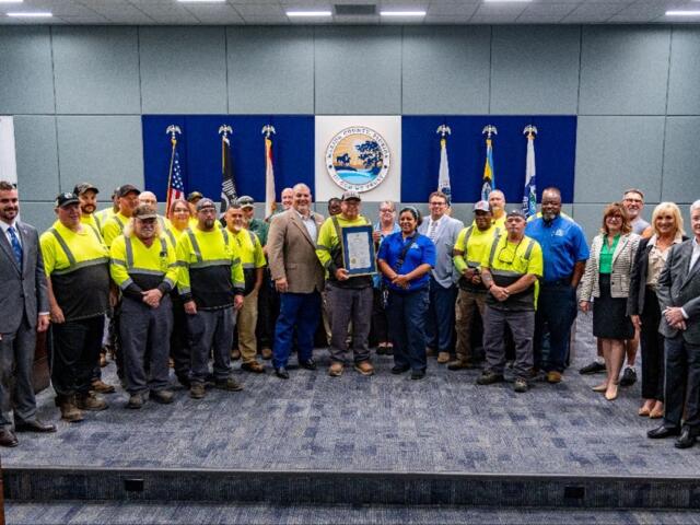 Marion County commissioners and Solid Waste staff gather in the commission chambers for a group photo, holding a framed proclamation honoring Waste and Recycling Workers Week.