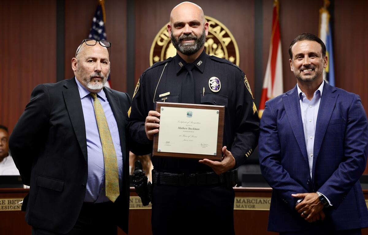 Officer Mathew Steckman holds a framed certificate while standing with Mayor Marciano and city staff.