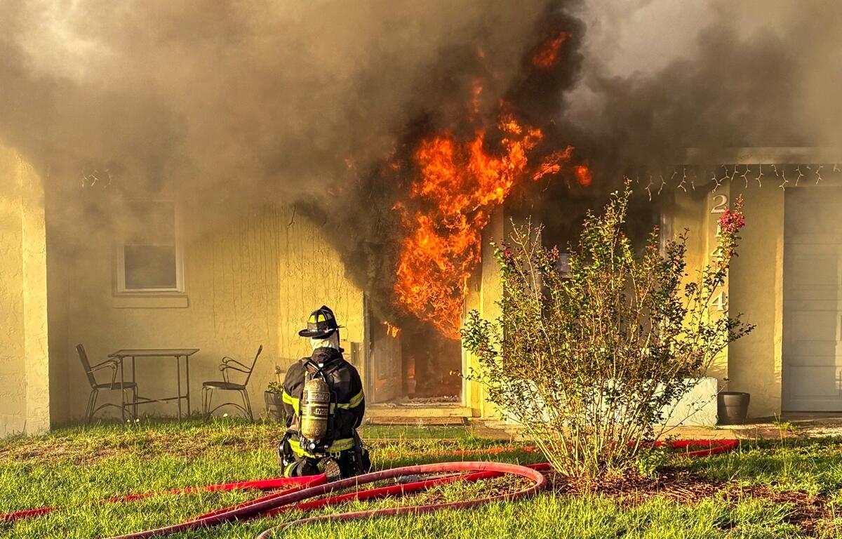 Firefighter kneels outside burning Dunnellon home as flames pour from doorway