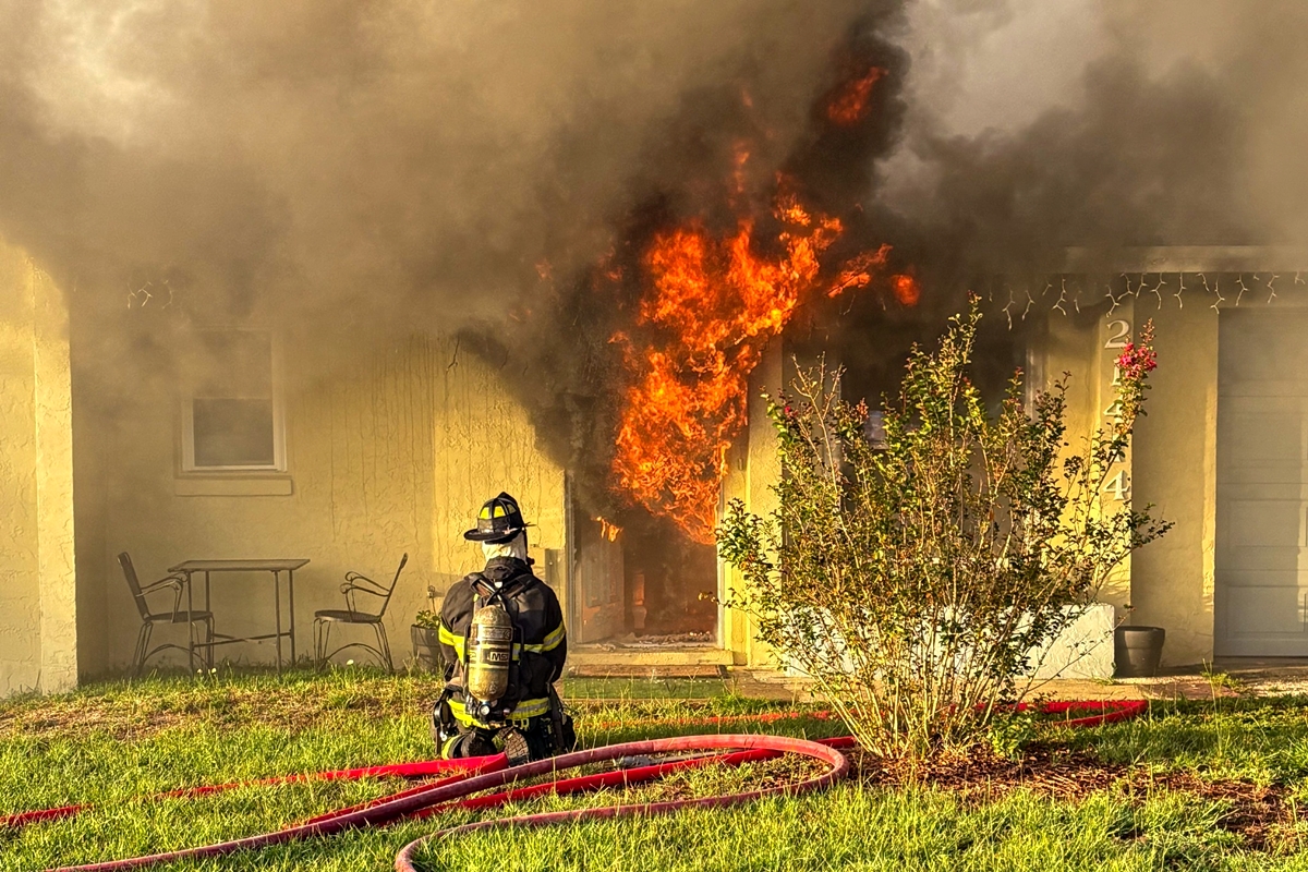 Firefighter kneels outside burning Dunnellon home as flames pour from doorway