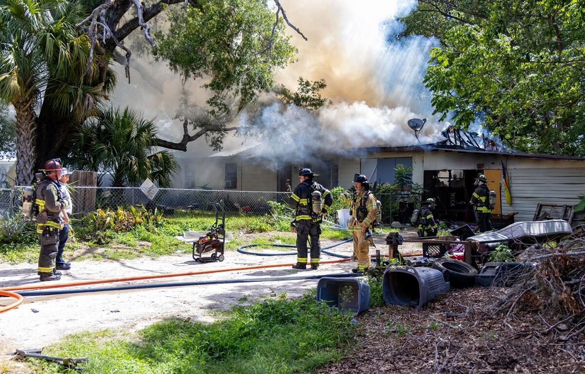 Several firefighters stand near debris and burned structure remains while assessing the aftermath of a house fire.