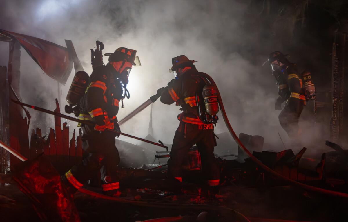 Firefighters are gathered near a fire engine, coordinating efforts or preparing equipment. The environment is still hazy with residual smoke. This image illustrates teamwork and emergency response coordination in the aftermath of the fire.