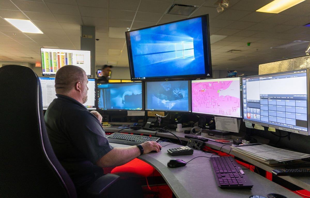 Dispatcher at Marion County 911 center monitors emergency call screens and maps at workstation.