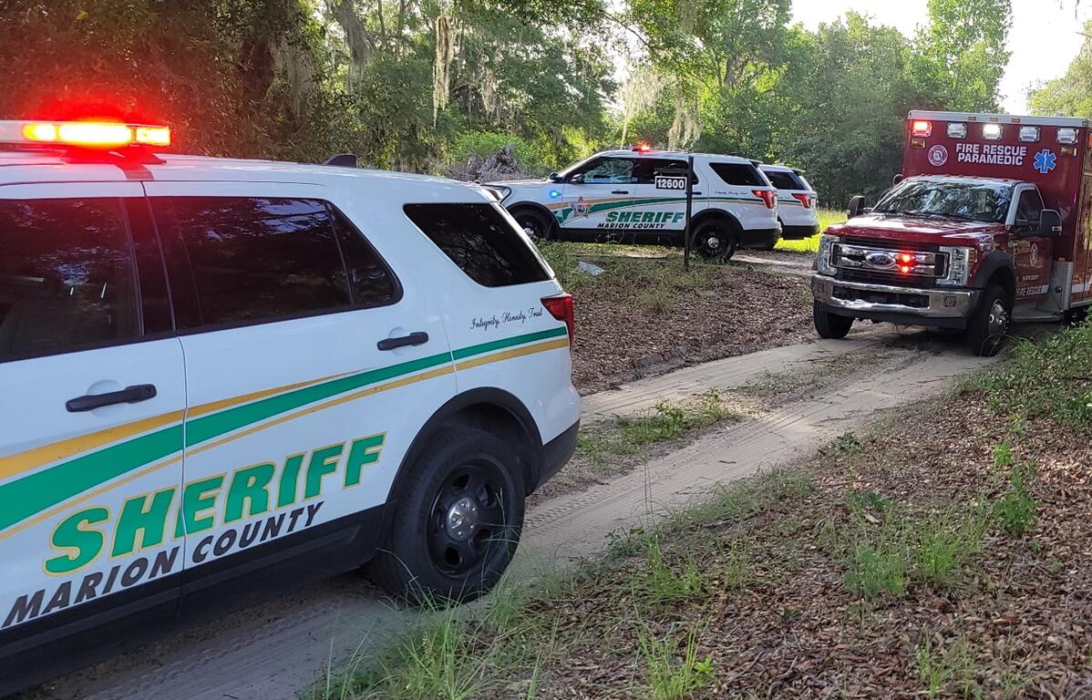 Marion County Sheriff's Office vehicles and a Fire Rescue ambulance parked on a dirt path during a shooting investigation in Anthony.