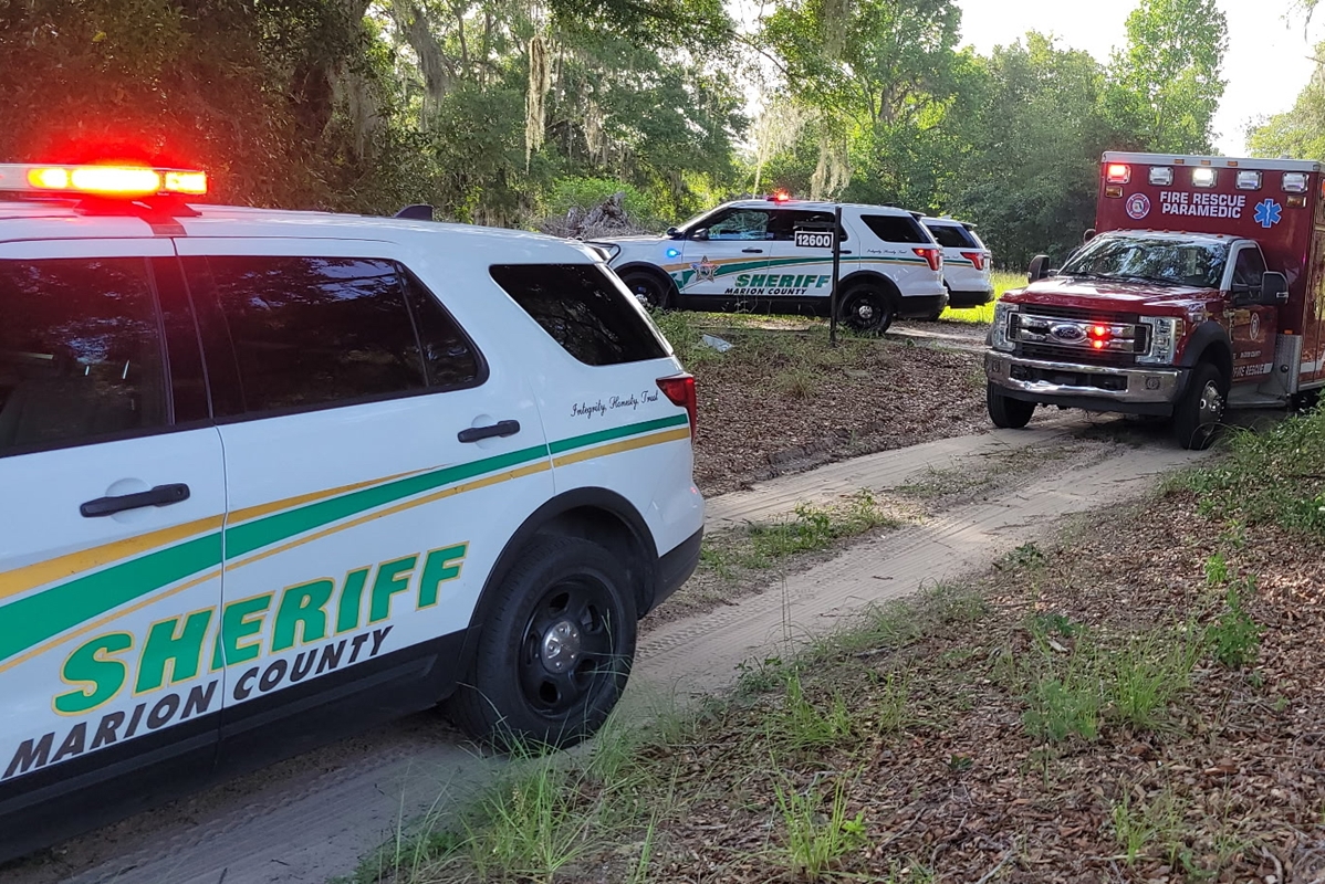 Marion County Sheriff's Office vehicles and a Fire Rescue ambulance parked on a dirt path during a shooting investigation in Anthony.