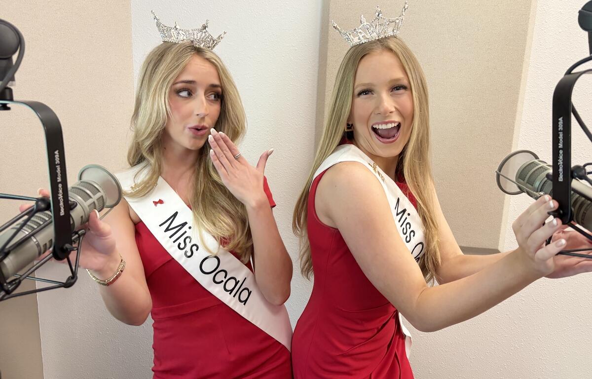 Miss Ocala 2025 Caroline Schapansky playfully covers her mouth while Miss Ocala Teen 2025 Madalyn Covington smiles and gestures toward a microphone in a radio studio.
