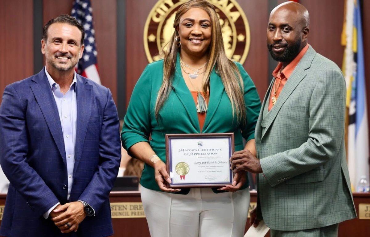 Ocala Mayor Ben Marciano stands with Darnitha and Larry Johnson holding a certificate at a city council meeting.
