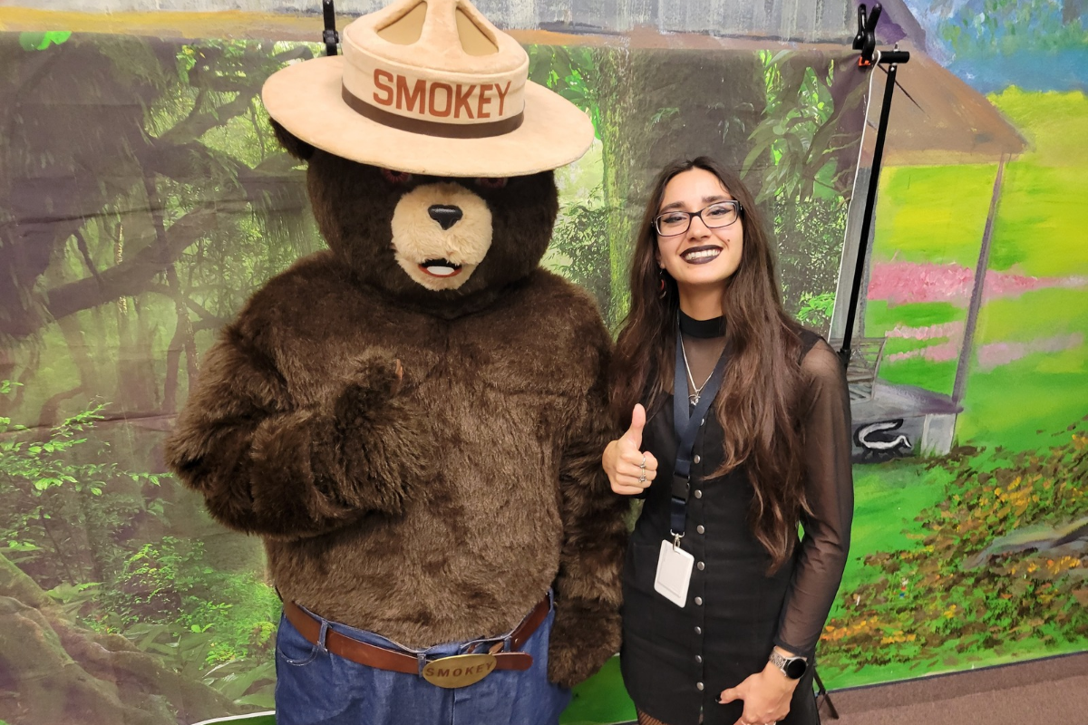 Smokey Bear stands next to reporter Ashley Brace, who is giving a thumbs up and smiling at the camera.