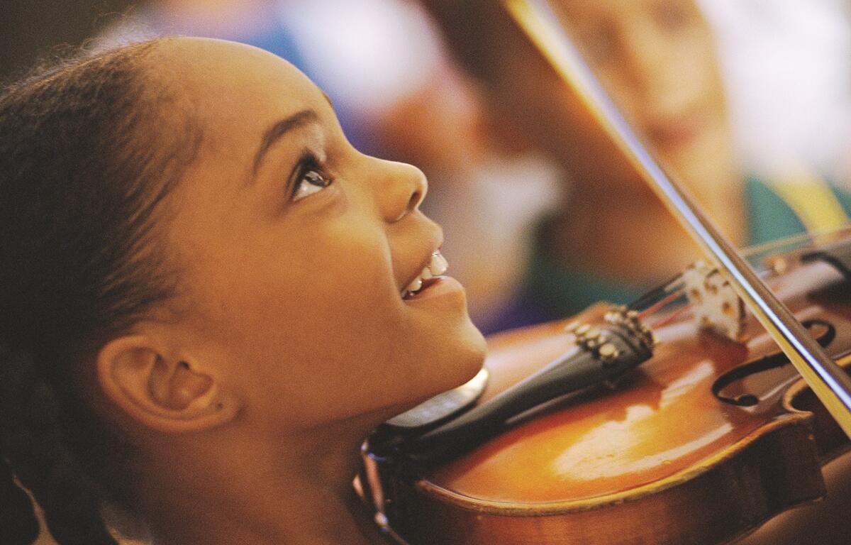 Child smiling while holding and playing a violin during a hands-on music camp.