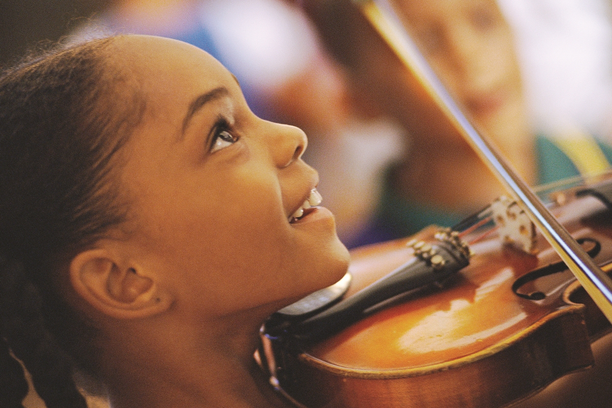 Child smiling while holding and playing a violin during a hands-on music camp.