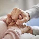 Close-up of a caregiver holding the hand of an elderly person, representing compassion and elder support.