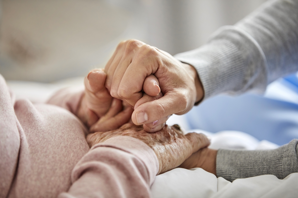 Close-up of a caregiver holding the hand of an elderly person, representing compassion and elder support.