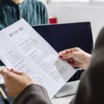 Hiring manager holding a résumé during an in-person job interview across a desk.