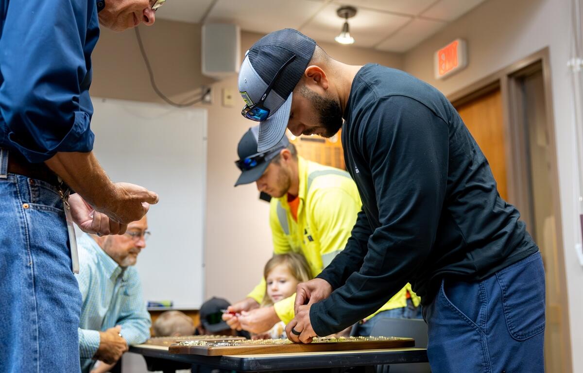 Gabriel Just-Rodriguez installs his nameplate on the Ocala Utility Services apprenticeship plaque while others look on during the June 2025 graduation event.