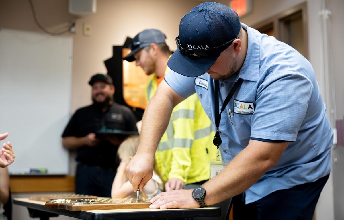 Ocala Utility Services graduate Chris Kennedy installs his nameplate on a recognition plaque during the June 2025 apprenticeship program ceremony.