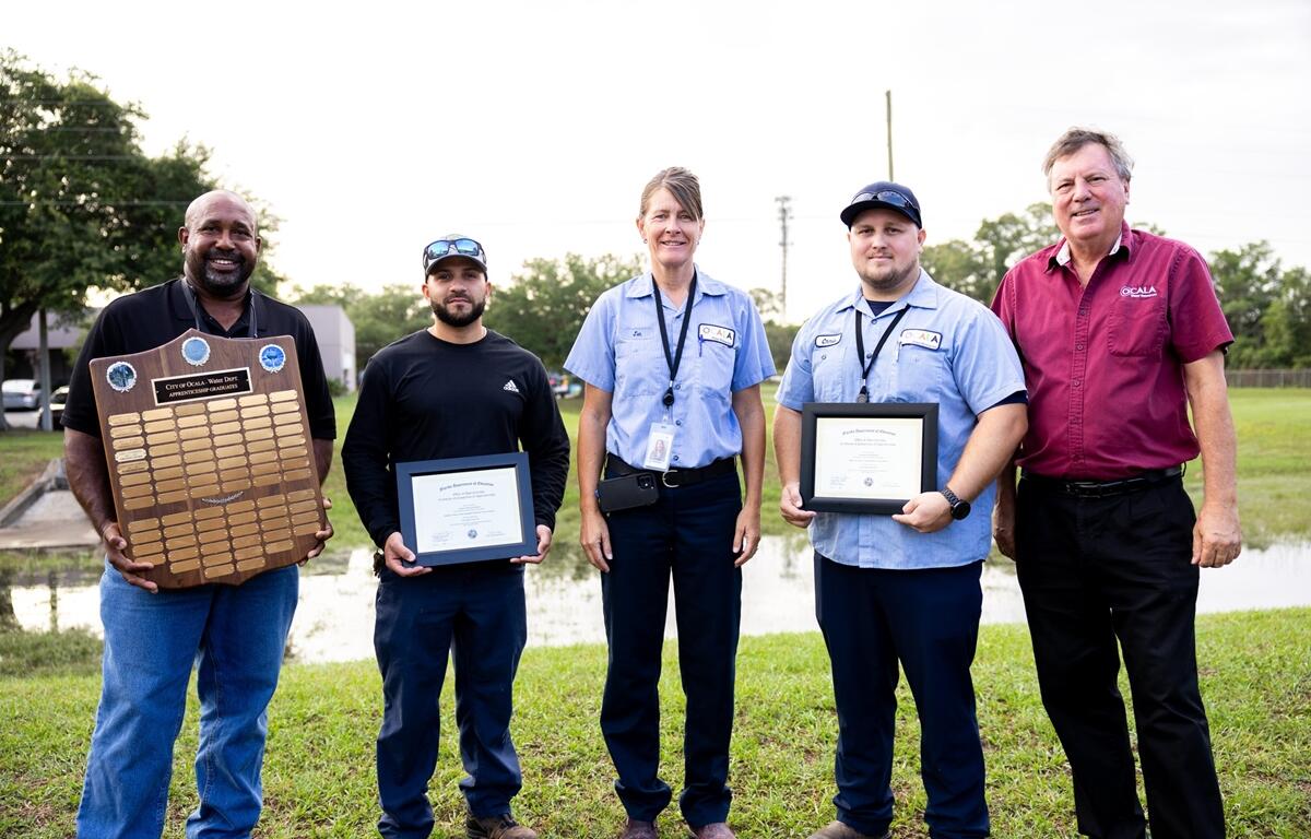 Group photo of Ocala Utility Services apprenticeship graduates and staff holding certificates and a plaque during a June 2025 recognition event.