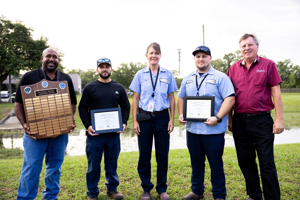 Group photo of Ocala Utility Services apprenticeship graduates and staff holding certificates and a plaque during a June 2025 recognition event.
