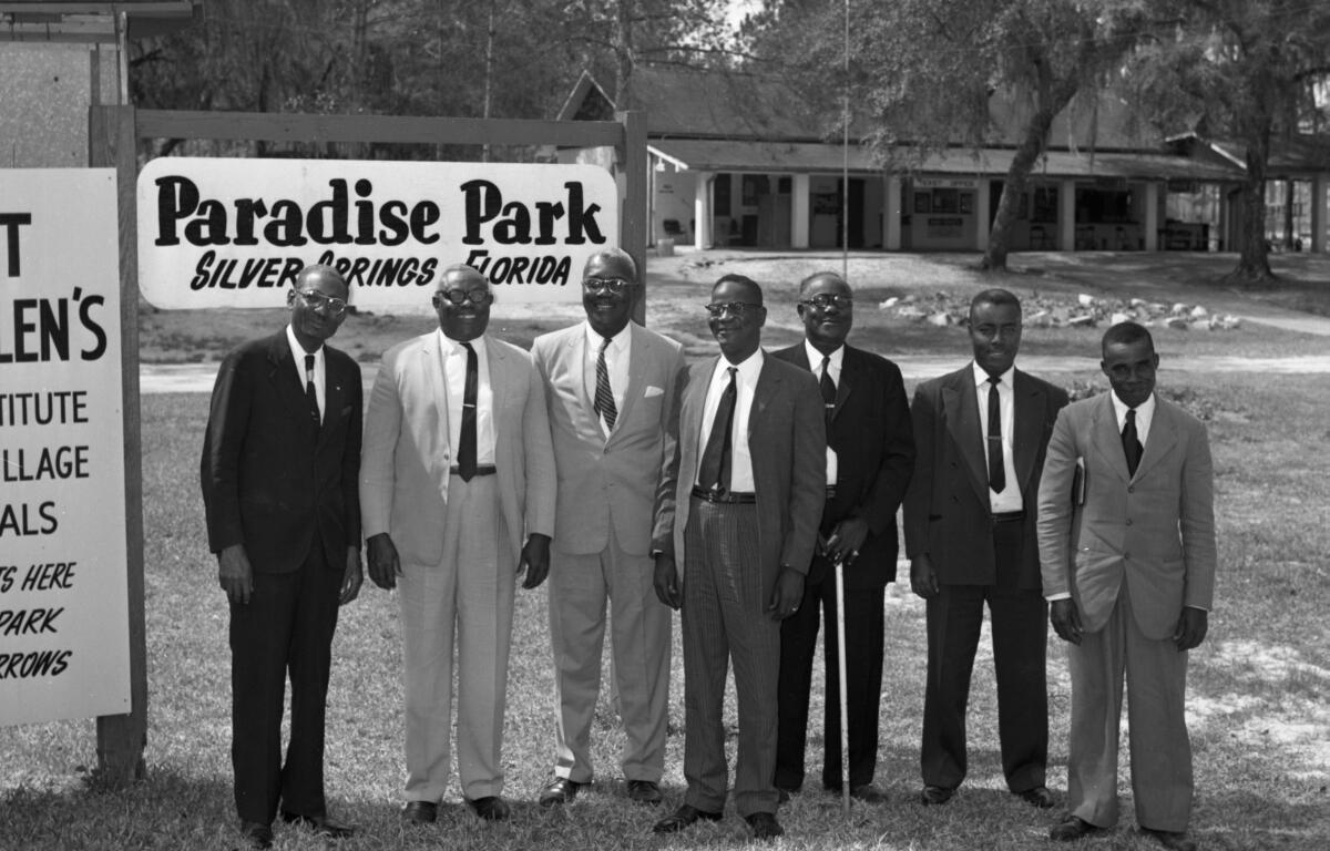Seven men in suits stand in front of the Paradise Park sign in Silver Springs, Florida, during the park's segregation-era operation.