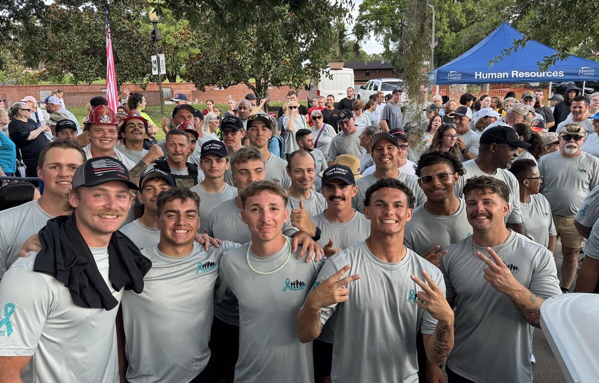 Smiling group of young men in PTSD Awareness Walk shirts pose in front of a crowd in Ocala.
