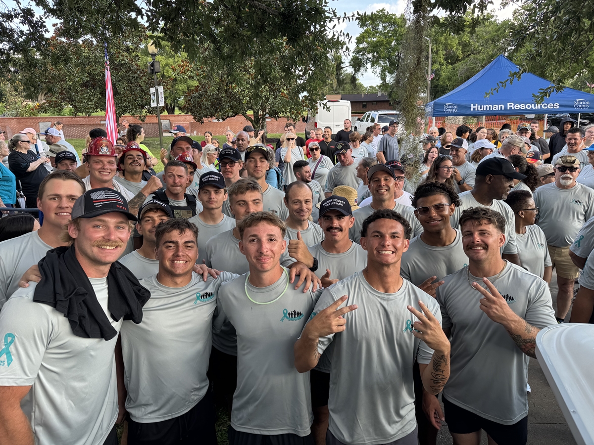 Smiling group of young men in PTSD Awareness Walk shirts pose in front of a crowd in Ocala.
