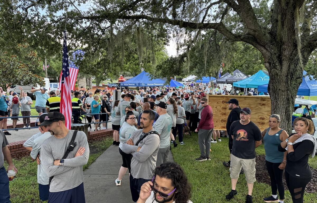 Large crowd gathered near vendor tents and shaded areas at the PTSD Awareness Walk in Ocala.